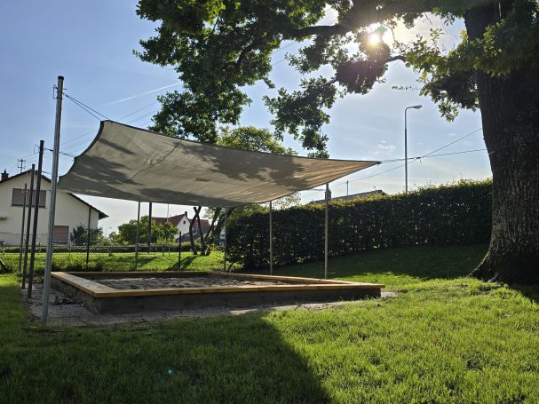 Sonnenschutz über einem Sandkasten in einer Gartenlandschaft.